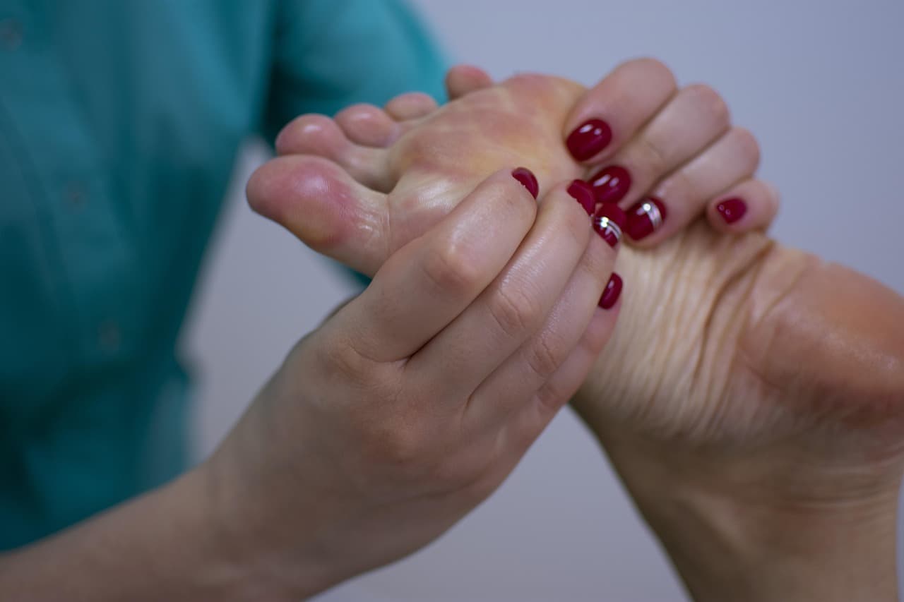 Hands with glossy deep red nails, one with a silver stripe, massaging the sole of a foot